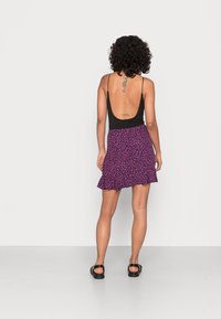 Mini-jupe fleurie violette avec un ourlet en volants, associée à un haut sans manches noir. Des sandales noires complètent la tenue.