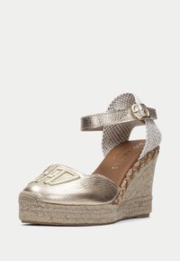 Metalické zlaté espadrilové sandály na klínu s tkaným bílým kotníkovým páskem, jute detaily a embosovaným vzorem na oblasti prstů.