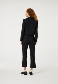 Zwarte op maat gemaakte cropped blazer met lange mouwen, gecombineerd met zwarte hoog ontworpen broek met een flared zoom. Slank ontwerp en een gladde textuur.