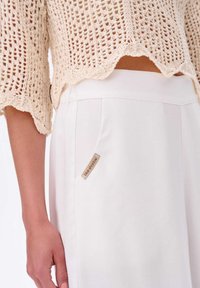 Gehaakte top in zacht beige met gegolfde randen, gecombineerd met witte broek met een zijlabel. Lichtgewicht materialen en gestructureerde ontwerpen.