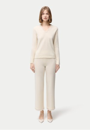 Cream pullover with a V-neck and ruffled trim, paired with wide-leg cream pants featuring fringe at the hem. Made of soft, textured material.