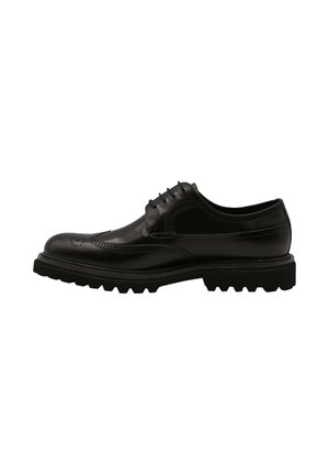 Chaussure brogue en cuir noir présentant un capuchon de chaussure surélevé, des perforations décoratives et une semelle épaisse et robuste pour une meilleure traction.
