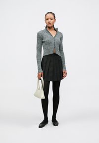 Pelēks ribots adīts rāvējslēdzēja kardigans, melna kroku mini svārki, melnas zeķubikses un melni plakanie apavi, kā arī mazs krēmkrāsas soma.