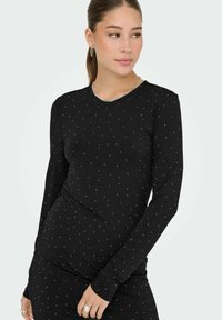 Svart långärmad topp med rund halsringning, prydd med ett spritt mönster av små silvernitar över tyget. Mjuk, figurnära design.