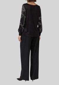 Schwarzes Longsleeve-Oberteil mit weißen abstrakten Linienmustern an den Ärmeln, kombiniert mit lockeren schwarzen Hosen und spitzen schwarzen Schuhen.