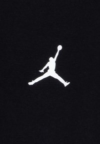 Zwarte stof met een witte Jordan-logo-silhouet, die een figuur in de lucht met een basketbal toont, waarbij atletische beweging en contrast worden benadrukt.