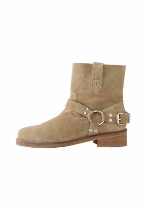 Tan suede ankle boot with a round toe, strap and ring detail, and a flat wooden heel. Features silver-tone hardware accents.