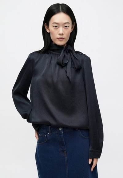 Blusa blu scuro in tessuto liscio, con fiocco al collo e bottoni decorativi su spalline e polsini.
