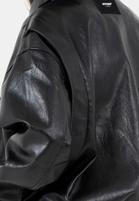 Zwarte leren jas met een gestructureerde afwerking, oversized mouwen en een label met "SIXTH JUNE PARIS" op de achterkant.