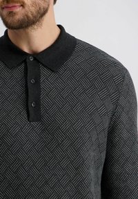 Schwarzes Poloshirt mit Muster und strukturiertem Gewebe. Der Kragen ist in solidem Schwarz mit drei Knöpfen, was das Design und das Material betont.