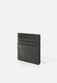 Portafoglio in pelle nera con un motivo a coccodrillo testurizzato e quattro slot per carte, in posizione verticale su una superficie bianca.