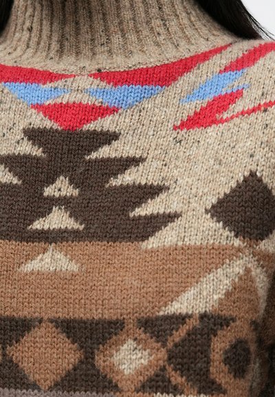Strikket sweater med høj halsudskæring, beige bundfarve og geometriske mønstre i rød, blå, brun og creme. Strukturen i garnet skaber dybde.