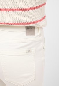 Weiße Jeans mit glatter Textur, ausgestattet mit einer Gesäßtasche mit einem kleinenLogo-Tag und einem Mustang-Logo-Patch am Bund.
