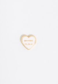 Gold-tone heart-shaped pin with embossed text "BIMBA Y LOLA" on a white enamel background. Smooth surface and polished edges.