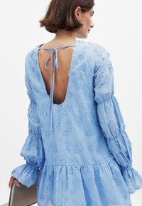 Svetlo modra vezenina obleka z globokim izrezom na hrbtu in trakovi. Ima napihnjene rokave, cvetlične vzorce in razširjen rob.