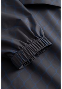 Sötétszürke szövet kék geometriai hálómintával és rugalmas mandzsetta részlettel az ujj részen.