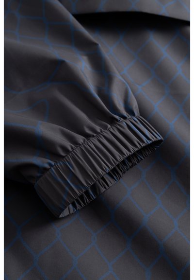 Tissu gris foncé avec un motif de grille géométrique bleu et détail de poignet élastique sur une manche.