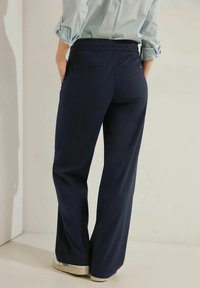 Marinblå vida byxor med en stretchmidja, två bakfickor och en slät tygkvalitet, kombinerat med ljusa skor.