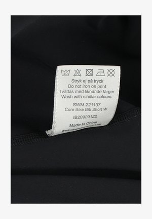 Sorte cykel bibshorts med et plejetikette, der har vaskeanvisninger, stofinformation og produktkode syet indvendigt.