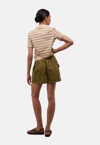 Polo à manches courtes rayé beige avec des rayures orange et marron, associé à un short vert olive et des sandales noires. Design simple et décontracté.