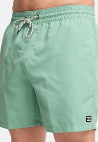 Costume da bagno verde menta realizzato in materiale leggero, con un elastico in vita e un laccetto bianco, e dettagli con tasche laterali.