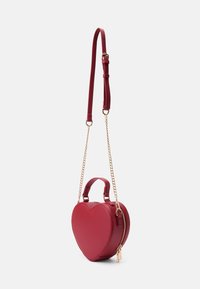 Sac à main en forme de cœur rouge en matériau synthétique, avec une fermeture à glissière, des poignées doubles et une bandoulière en chaîne amovible. Accompagné d'accents dorés.