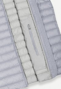 Világosszürke steppelt dzseki réteg látható cipzárral és függőleges cipzáras mellzsebbel a belső bélésen.