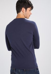 Navy long-sleeve shirt in a smooth, lightweight fabric with a classic crew neckline and a fitted shape, paired with blue jeans.