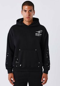 Zwarte hoodie van katoenmix. Voorzien van een witte spetterdesign op de mouwen en de voorzak, met metalen studs als accenten.