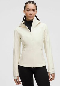 White zip-up jacket with a fitted design, featuring a hood, two side pockets, and subtle stitching details. Black high-neck top underneath.