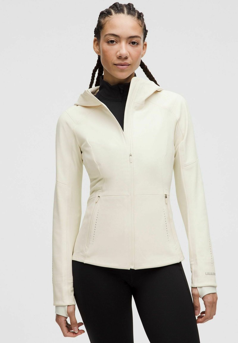 White zip-up jacket with a fitted design, featuring a hood, two side pockets, and subtle stitching details. Black high-neck top underneath.