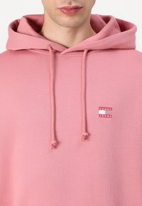 Felpa rosa realizzata in tessuto morbido con etichetta logo frontale. Presenta un cappuccio con cordino e una vestibilità comoda.