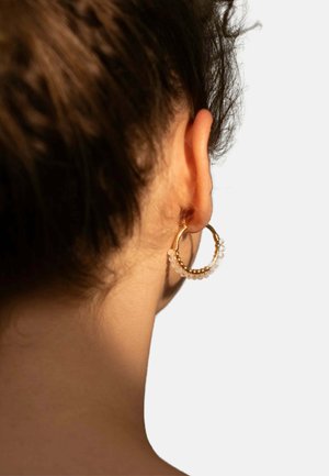 Orecchini a cerchio in oro con un design testurizzato e una fila di piccole perline traslucide lungo il bordo inferiore. Lo sfondo è neutro.