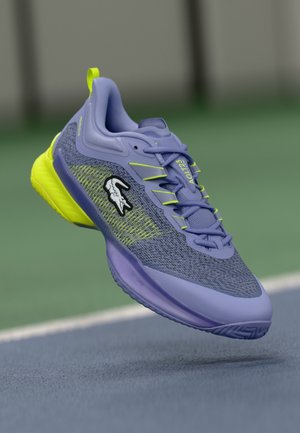 Lacoste sportiniai batai levandų ir neoninės geltonos spalvos. Turi kvėpuojančią aulo viršutinę dalį, tekstūruotą padu ir logotipo akcentą šone.