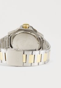 Silber- und goldfarbene Armbanduhr mit einem Edelstahlarmband, runder Gehäuseform und einer hervorstehenden Krone mit strukturiertem Griff bei 2 Uhr.