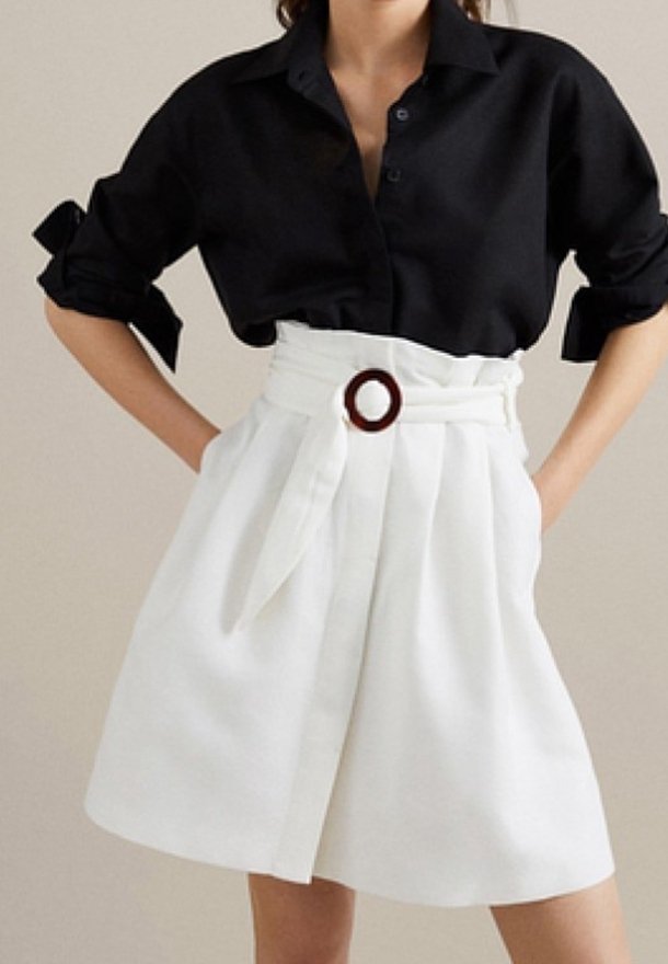 Donna che indossa una blusa nera a maniche lunghe con maniche arrotolate e una gonna bianca a vita alta con una cintura larga e una fibbia rotonda.