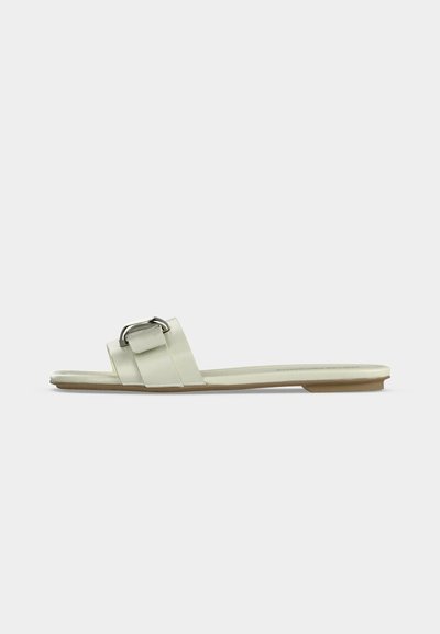 Sandale slide blanche avec large bride et boucle argentée, semelle plate et semelle extérieure beige, vue de profil sur fond neutre.