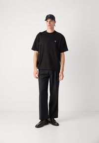 T-shirt nera con un piccolo logo, pantaloni neri e un cappellino abbinato. Il look è completato da scarpe stringate nere e una tracolla.