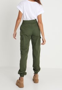 Gröna cargobyxor med elastiska muddar och sidofickor, tillsammans med en vit kortärmad skjorta. Outfiten har en avslappnad passform och en avslappnad stil.