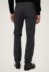 Tmavě šedé kalhoty s úzkým střihem, s hladkou texture a dvěma zadními kapsami. Nosené s hnědými vyleštěnými botami.