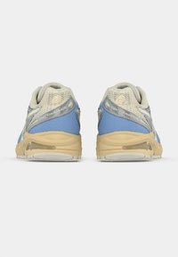 Ténis de corrida com parte superior em rede azul e cinza, sola de borracha bege e colarinho acolchoado para maior conforto. Logótipo notável na lateral.