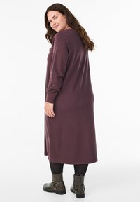 Duga, uska haljina od tkanine tamnopurpurne boje s dugim rukavima, do sredine lista. Uparena s crnim tajicama i gležnjačama s ukrasnim remenčićima.