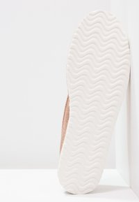 Scarpa flat con una suola in gomma bianca testurizzata e una parte superiore morbida in rosa dorato metallizzato. Il design è semplice e minimalista con una finitura liscia.
