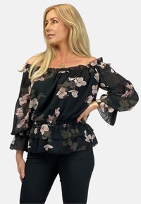 Czarna bluzka bez ramiączek z kwiecistym wzorem, z falbaniastymi rękawami i fasonem peplum. Posiada różowe i zielone kwiatowe wzory na przezroczystym materiale.