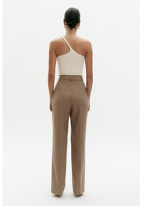 Geribbelde crèmekleurige top met één schouder, gecombineerd met hooggesneden, beige wijde broek, wat een gestroomlijnd silhouet en een soepele textuur creëert.