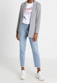 Grå kavaj, vit grafisk t-shirt med röd text, ljusblå cropped jeans, vita sneakers. Kavajen har långa ärmar och slag.