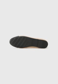 Suola di una scarpa caratterizzata da un fondo in gomma nera con scanalature orizzontali, posizionata su un materiale superiore di un beige chiaro.