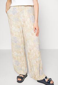 Person som bär lätta, pastelliga blommiga vida byxor med elastisk midja och marinblå plattformssandaler med spännen, stående mot en vit bakgrund.