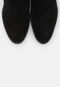 Bottines noires en daim avec un bout arrondi et une texture lisse, présentant des coutures et un design élégant.