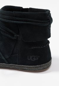 Černé semišové kotníkové boty s překládaným designem, prošitými detaily a gumovou podšívkou se strukturovaným okrajem. Logo UGG na boku.